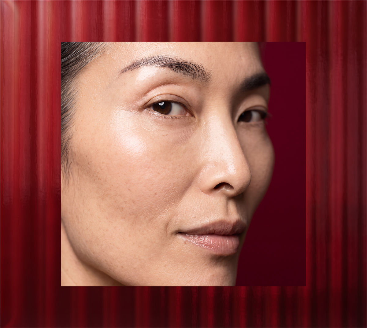 Close-up portrait of a woman with smooth facial skin against a deep red textured background
