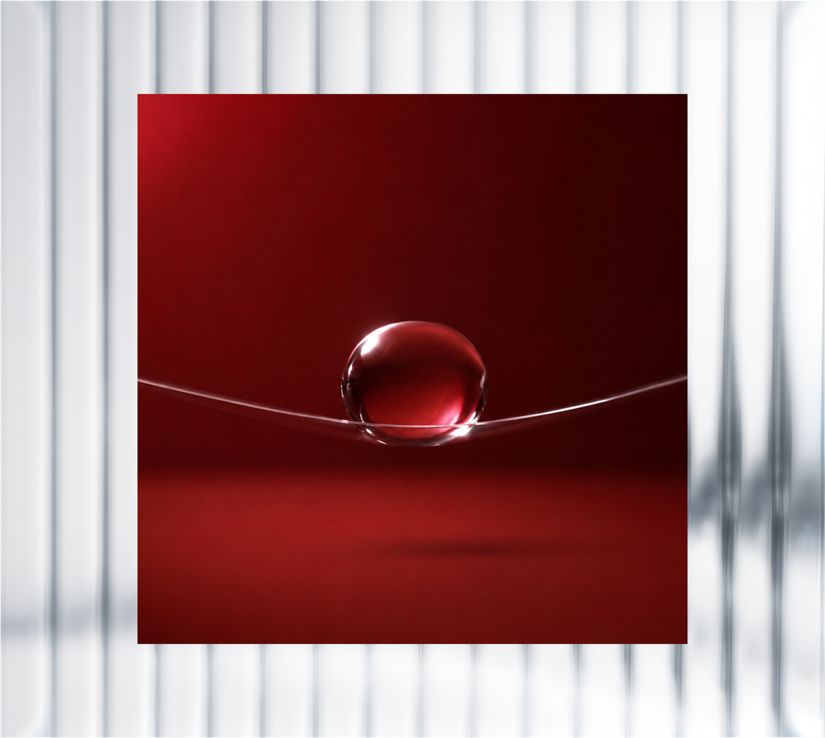 Glossy red serum droplet resting on a curved surface against a deep burgundy background