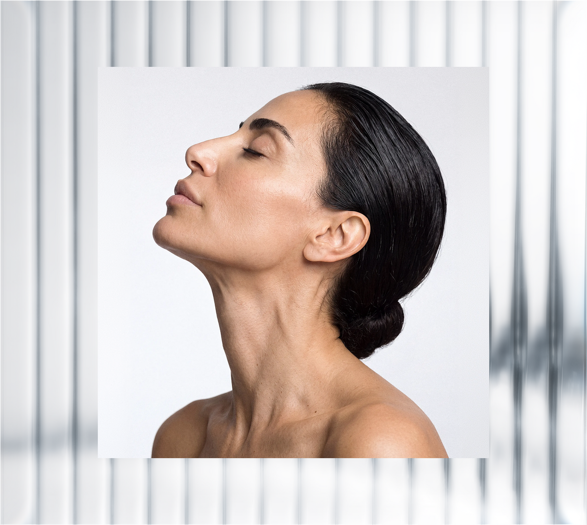 Side profile of a woman with dark hair tied in a bun, showing smooth facial skin and neck against a light background