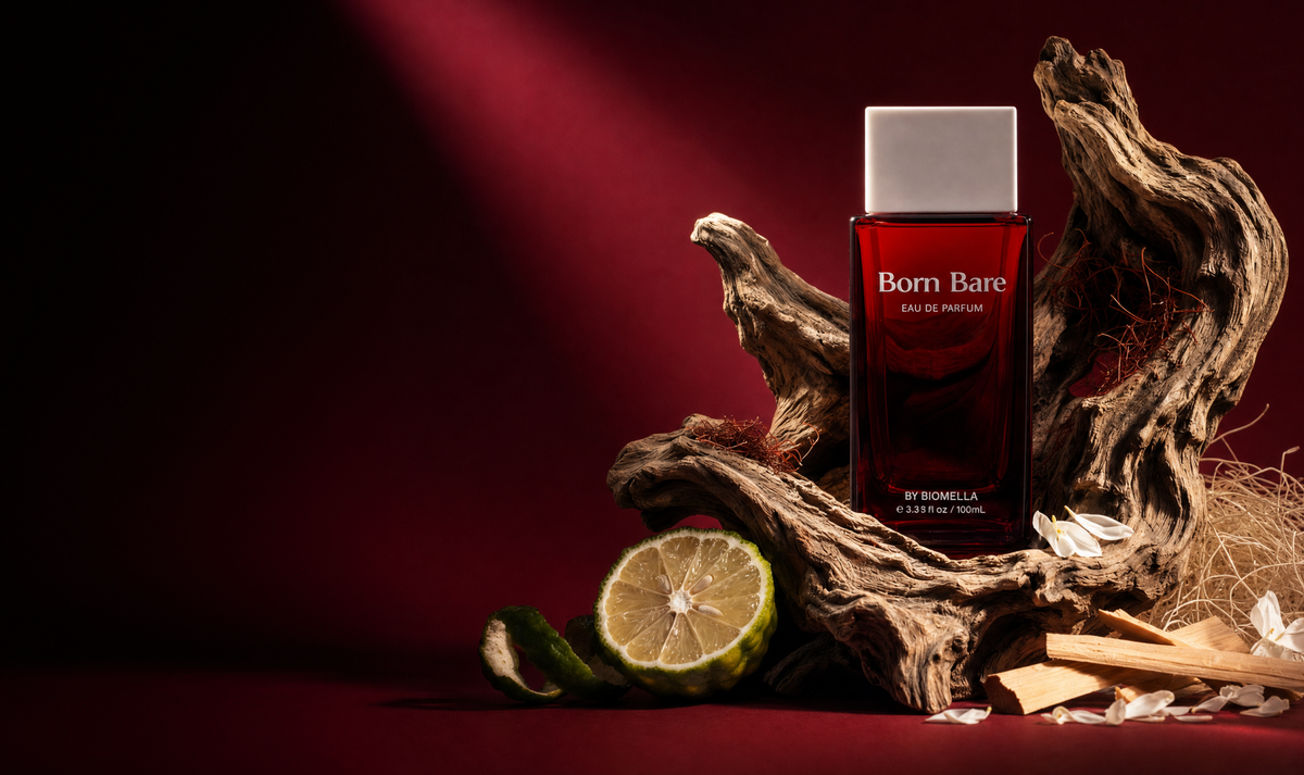 Biomella Born Bare Eau de Parfum red perfume bottle surrounded by driftwood, bergamot, and sandalwood against a dark red background