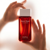 Hand holding Biomella Born Bare Eau de Parfum red perfume bottle against a white background