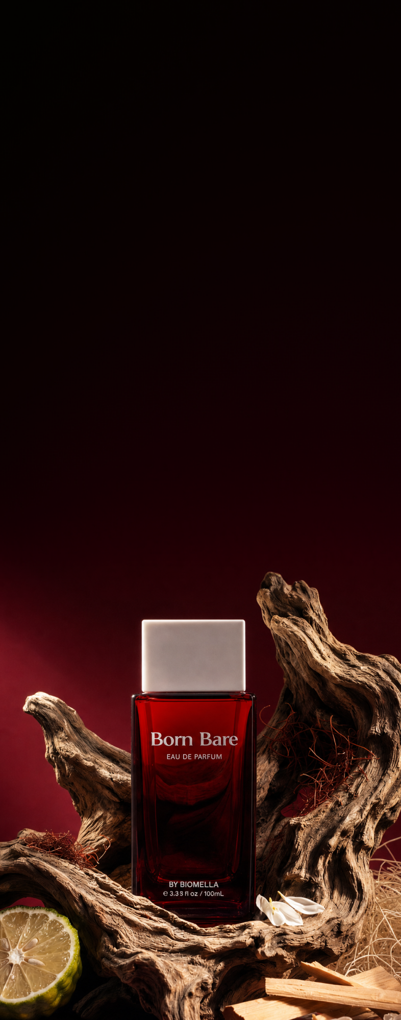 Biomella Born Bare Eau de Parfum red perfume bottle surrounded by driftwood, bergamot, and sandalwood against a dark red background