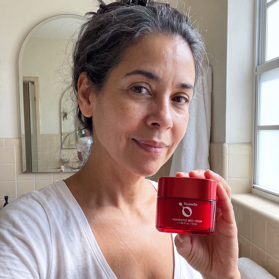 Woman with dark hair holding a red jar of Biomella Postbiotic Neck Cream